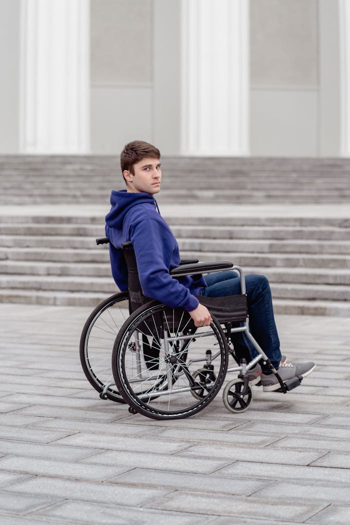 A young man in a wheelchair wearing a hoodie outdoors on steps. Urban setting.